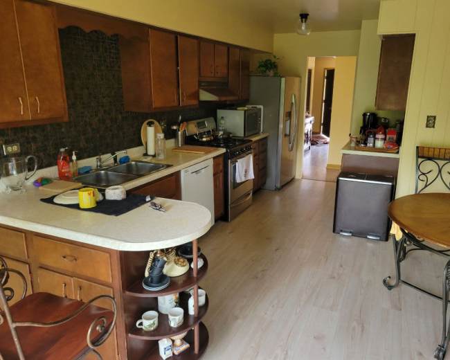 The image shows a kitchen with wooden cabinets, a gas stove, a sink, and a dining table in the corner.