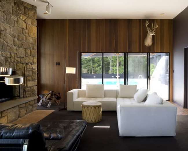 A modern living room with a stone fireplace, a white sectional sofa, and large windows overlooking a pool area.