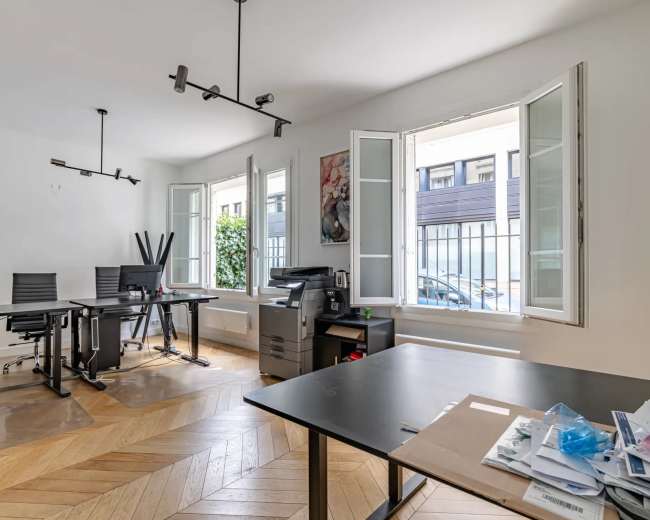 The image shows a modern office space with several black chairs, desks, and large windows that open to a street view.