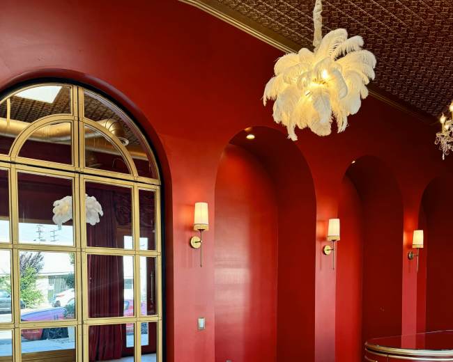 A red-walled interior with arched doorways, a mirrored wall, and a decorative reception desk in a herringbone-patterned wooden floor.