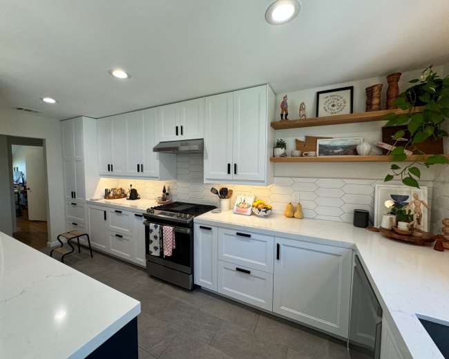 A modern kitchen with white cabinets, a stainless steel stove, and a hexagonal tile backsplash, featuring decorative items on the shelves.