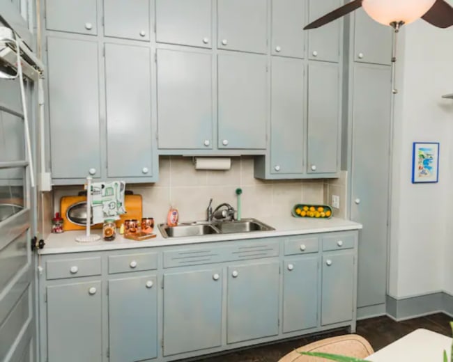 A small kitchen with gray cabinets, a sink, a countertop, and a black stove.