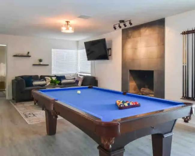 A game room featuring a blue pool table, a fireplace, a mounted television, and a seating area with a couch.