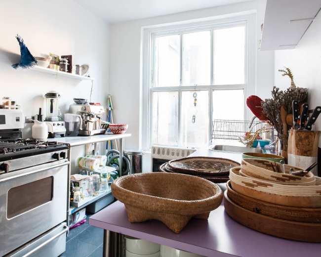 A modern kitchen features stainless steel appliances, open shelving with various kitchen items, and bamboo bowls on a purple countertop.