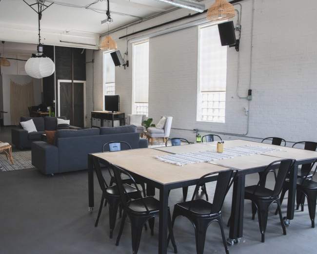 The image shows a spacious, modern interior featuring a large dining table, upholstered seating areas, and minimalist decor in a well-lit room.