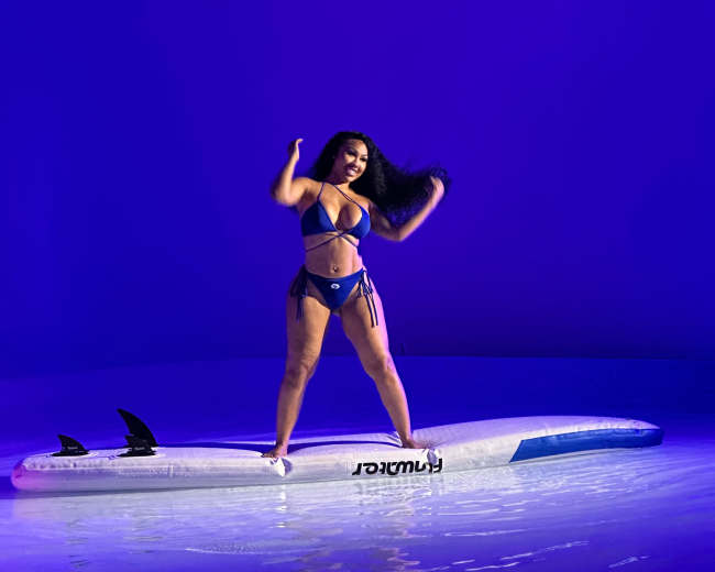 A person stands on a surfboard in a pool of water under blue lighting.