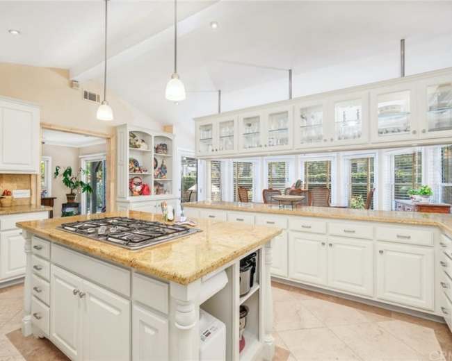 The kitchen features white cabinets, a central island with a gas cooktop, and large windows providing ample natural light.