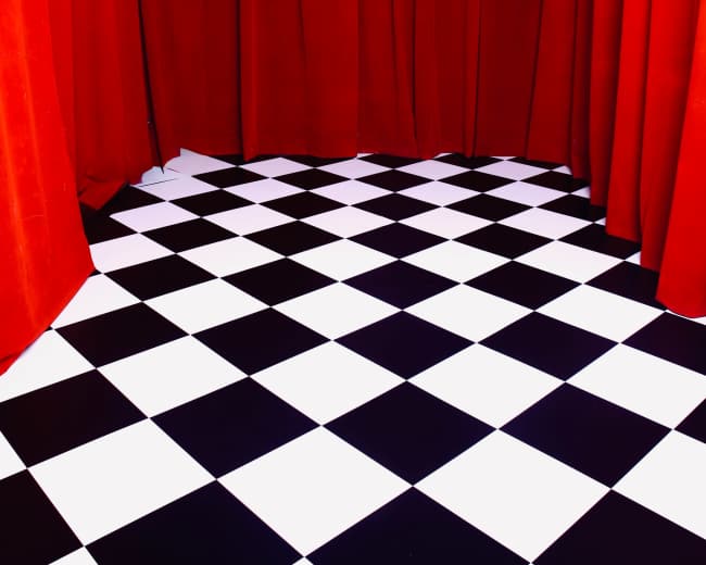 The image shows a stage area with red curtains and a black and white checkered floor.