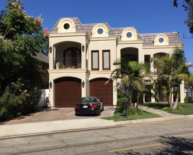 A large, two-story house with a tile roof and a dark sedan parked in front of the garage.