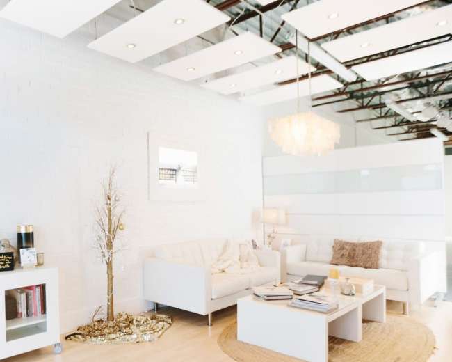 The image shows a bright, modern living room with white furniture, a circular rug, and a decorative tree.