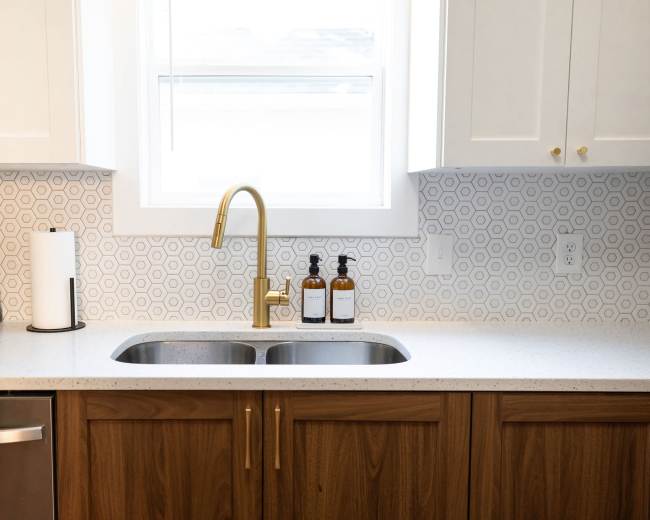 A modern kitchen features a double sink with a gold faucet, surrounded by white cabinets and a hexagonal patterned backsplash.