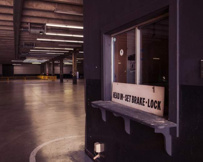 The image shows an empty warehouse interior with a window labeled "READ IN-SET BRAKE-LOCK" and fluorescent lights overhead.