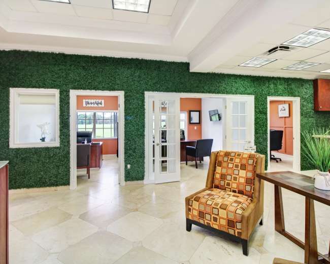 An office reception area featuring a green wall, two glass doors leading to additional rooms, and a seating area with a patterned chair.