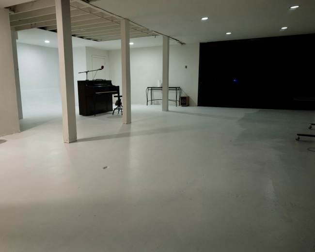 A spacious, minimalist room with white walls, a polished floor, and a piano placed against one wall.