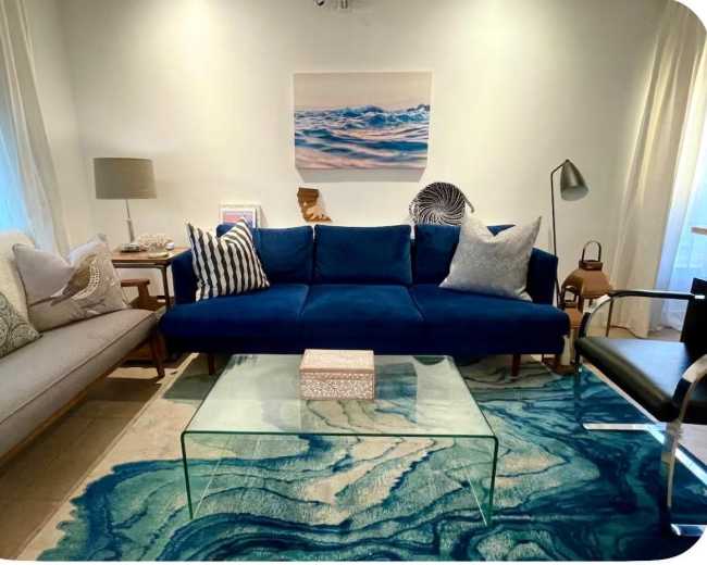 The image depicts a modern living room with a blue couch, a glass coffee table, and decorative elements like cushions and artwork.