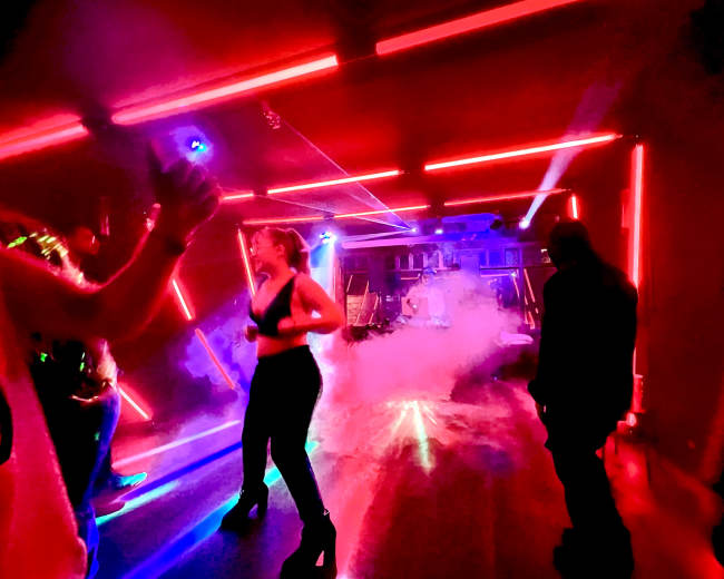 A group of people dances under neon lights in a smoke-filled room.