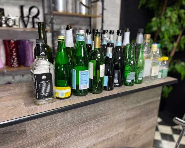 A row of empty and partially filled glass bottles of various shapes and sizes is lined up on a bar counter.