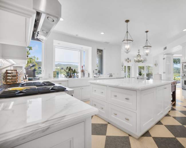The image features a modern kitchen with a large marble island, white cabinetry, and a checkerboard floor design.