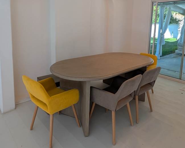 A round dining table surrounded by four chairs, with two in light gray and one in yellow, set against a white wall with archways.