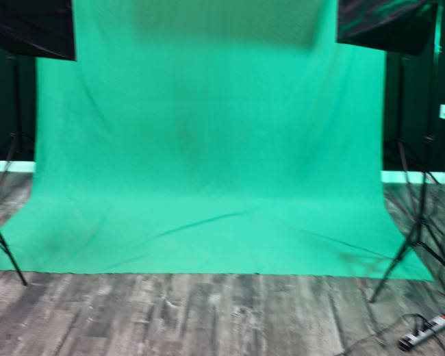 A green screen setup is positioned between two softbox lights in a studio environment.