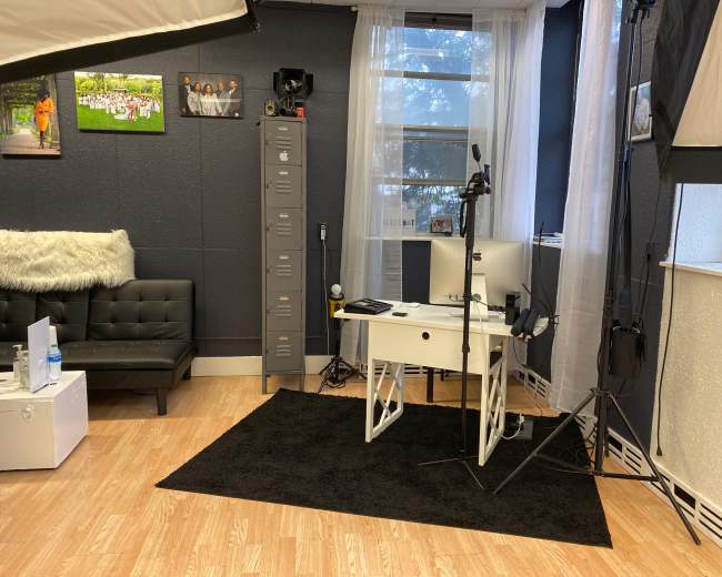 The image shows a modern workspace with a black sofa, a desk with a computer, and photography equipment in a well-lit room.