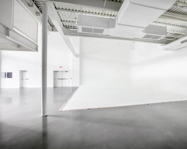 A spacious, empty room with white walls and a polished concrete floor, featuring a slightly raised white surface at one end.
