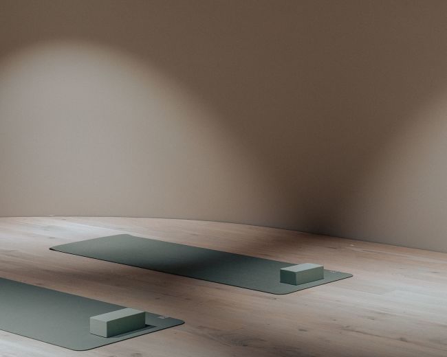 The image shows two yoga mats placed on a wooden floor in a dimly lit room with a brown wall.