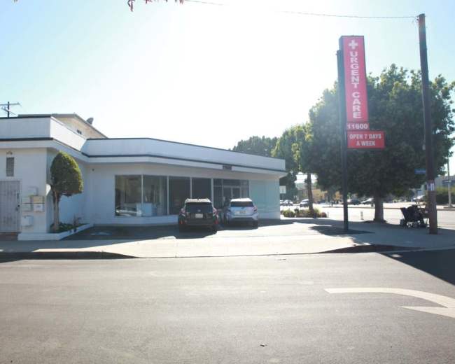 A single-story medical facility marked as "Urgent Care," featuring a large sign, situated on a street corner with several parked cars nearby.
