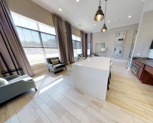 A modern interior space with a light-colored kitchen island, gray seating, large windows, and hardwood flooring.