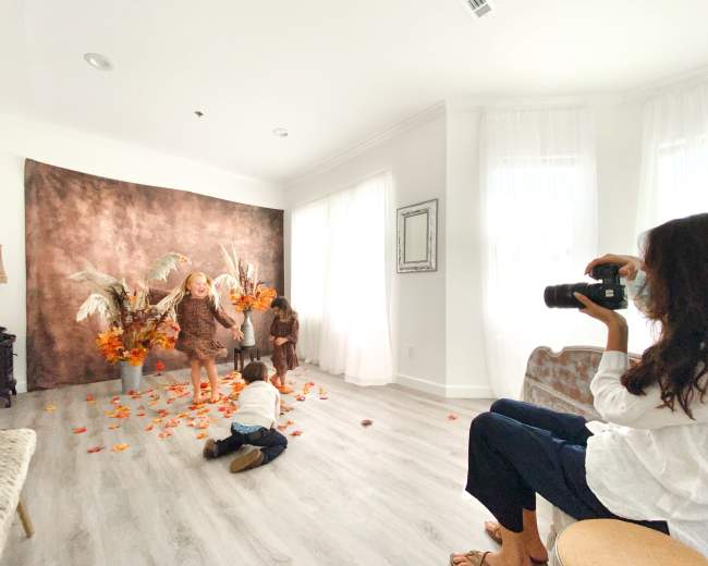 A photographer captures children playing among autumn-themed decorations in a brightly lit room.