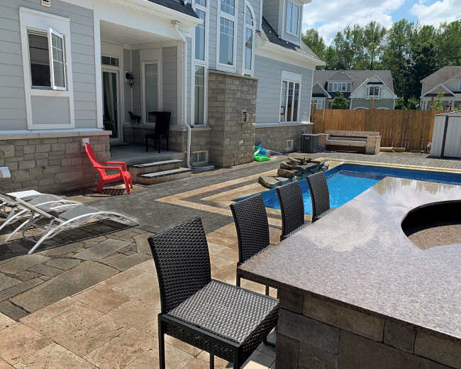 The image shows a residential backyard with a swimming pool, a stone patio, outdoor seating, and a house in the background.