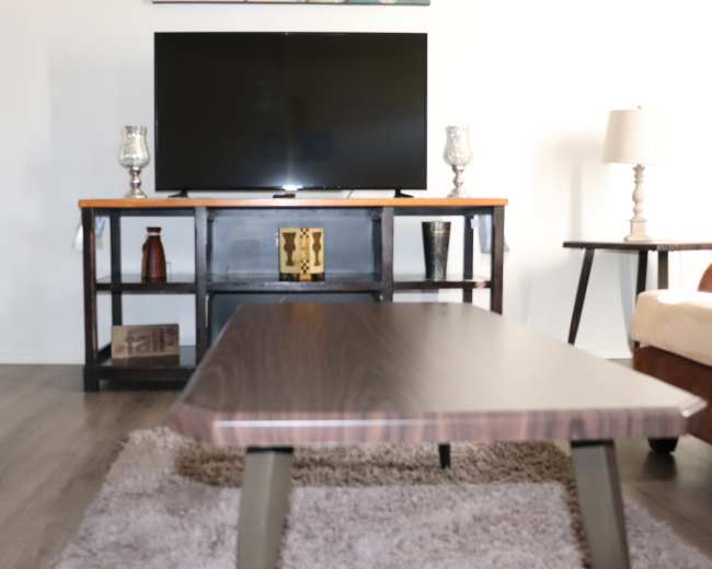 The image shows a living room with a television on a stand, a coffee table in front of it, and various decorative items on shelves.