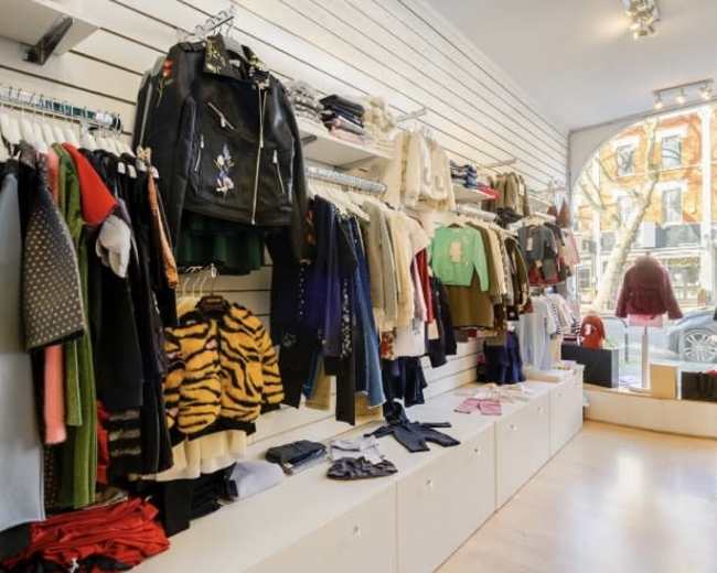 The image shows a clothing retail store with various garments displayed on wall racks and shelves, and a large window facing the street.
