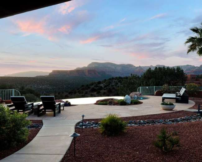 A patio with lounge chairs overlooks a desert landscape and mountains under a twilight sky.