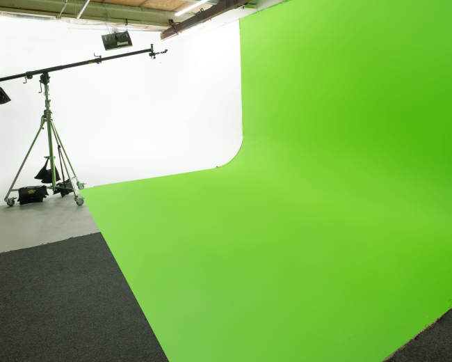 The image shows a photography studio with a green screen backdrop, a white wall, and a lighting rig on a stand.
