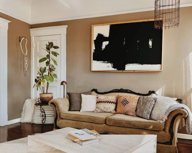 The image shows a cozy living room with a vintage sofa, a coffee table, and a large abstract painting on the wall.