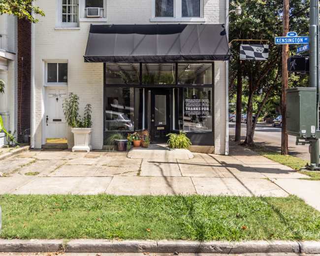 The image shows a two-story building with a black awning over the front entrance and a manicured sidewalk, located at the corner of Kensington Street.