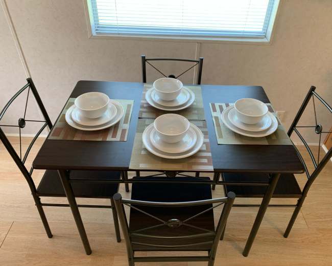 A dining table set for four with plates, bowls, and placemats, situated in a well-lit room.
