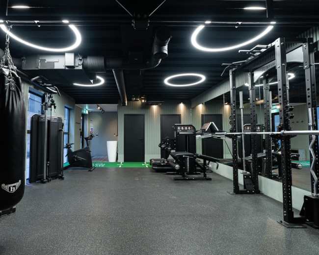 The image shows a modern gym equipped with a punching bag, strength training racks, and various fitness machines, featuring sleek black and green decor.
