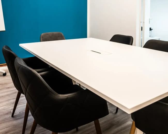 The image shows a modern conference room with a large white table surrounded by black chairs and a blue accent wall.
