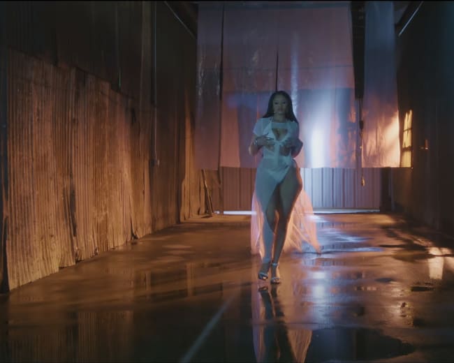 A woman walks through a narrow, dimly lit corridor with reflective wet floors and industrial walls.