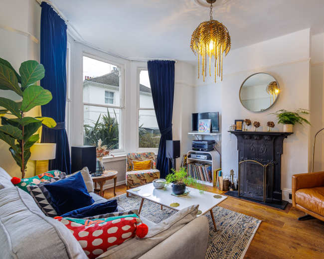 The living room features a mix of comfortable seating, a fireplace, and large windows with blue curtains, creating a cozy atmosphere.