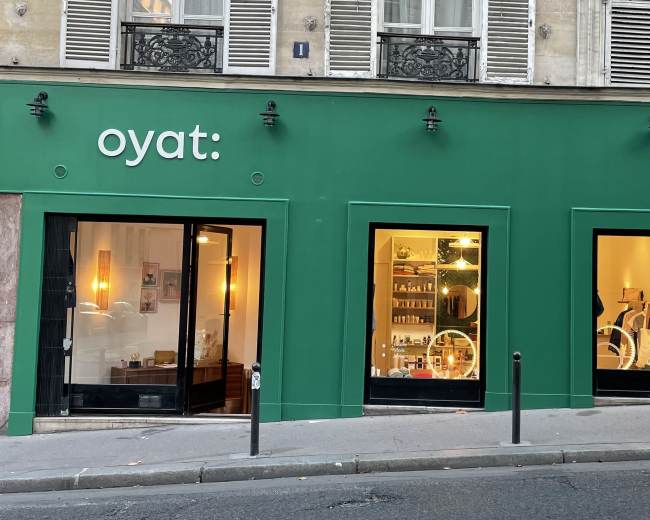 The storefront features a bright green facade with three large windows displaying various products and clothing inside.