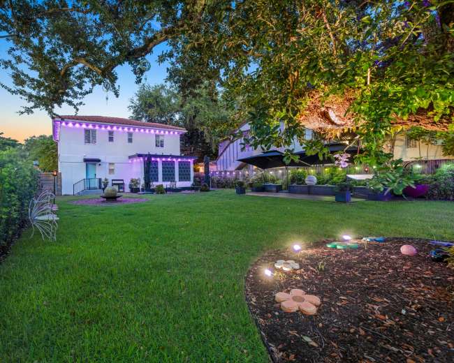 The image shows a two-story white house with outdoor lighting, surrounded by a green lawn and landscaped areas.