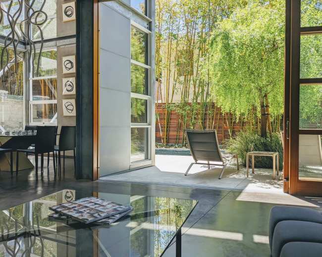 A modern living space features large glass doors opening to a serene outdoor area with bamboo and lounge chairs.