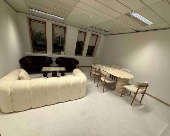 The image shows a minimalist office space with a curved couch, a small glass coffee table, and a round dining table surrounded by chairs.