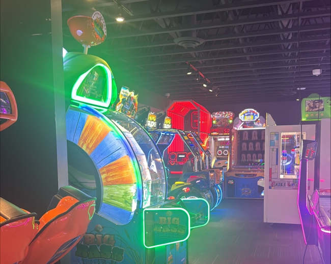 The image shows a brightly lit arcade filled with various colorful gaming machines and attractions.