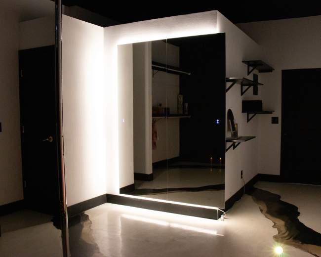 A modern room with a large mirror, minimal shelving, and a unique floor design featuring a wavy pattern.