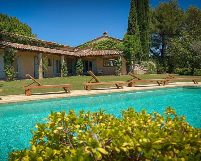 The image shows a serene villa beside a swimming pool surrounded by lounge chairs and lush greenery.
