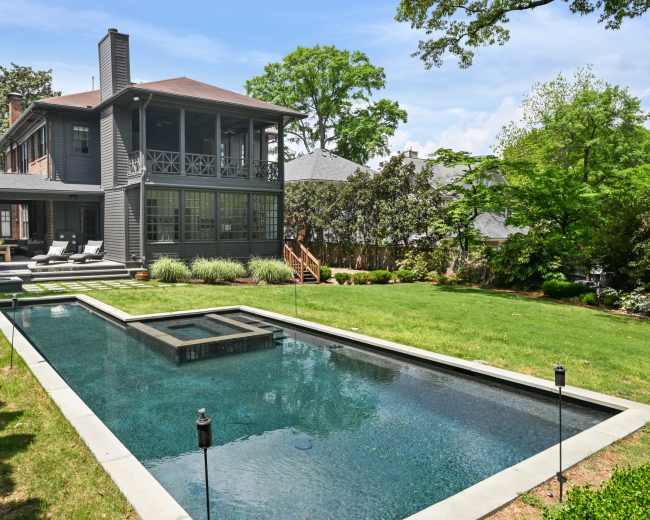 A two-story gray house with a spacious backyard features a rectangular swimming pool and landscaped greenery.